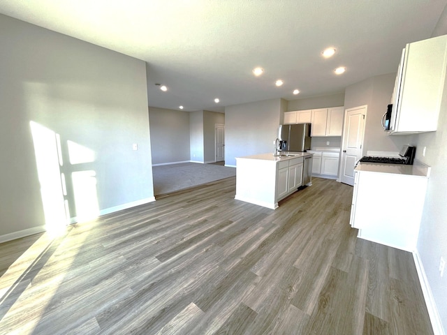 kitchen with sink, light hardwood / wood-style flooring, a kitchen island with sink, white cabinetry, and stainless steel appliances