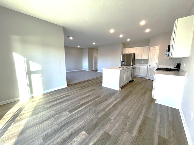 kitchen featuring sink, appliances with stainless steel finishes, white cabinetry, light hardwood / wood-style floors, and an island with sink