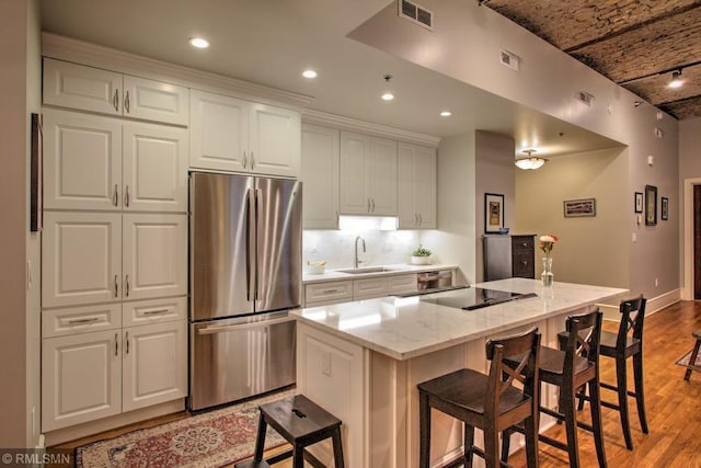 kitchen with a kitchen island with sink, white cabinetry, stainless steel fridge, and light stone countertops