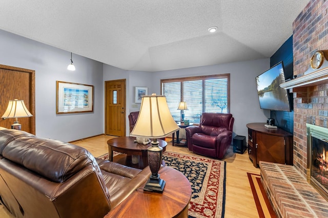 living room with vaulted ceiling, light wood-type flooring, a brick fireplace, and a textured ceiling