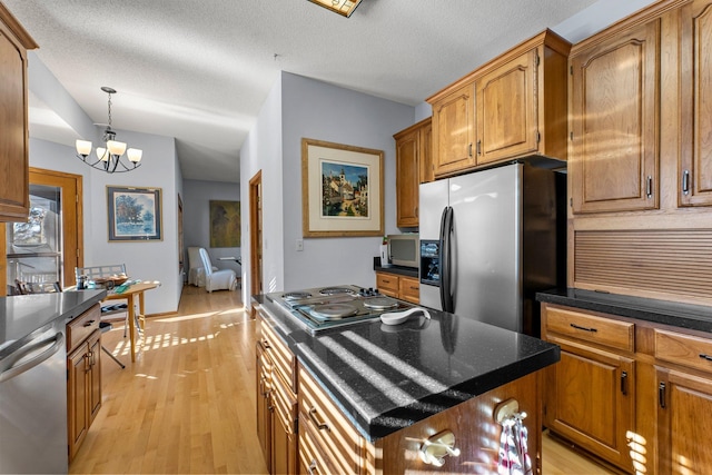 kitchen with a kitchen island, appliances with stainless steel finishes, a notable chandelier, a textured ceiling, and light hardwood / wood-style flooring