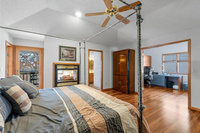 bedroom featuring ceiling fan, ensuite bathroom, a multi sided fireplace, light hardwood / wood-style floors, and a textured ceiling