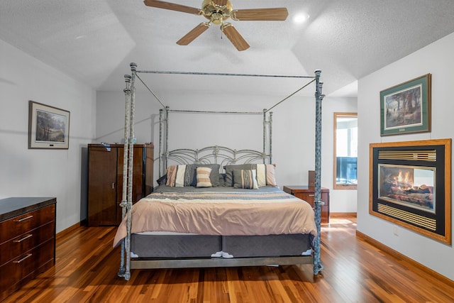 bedroom with vaulted ceiling, a textured ceiling, a multi sided fireplace, dark hardwood / wood-style flooring, and ceiling fan