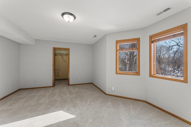 unfurnished bedroom featuring a walk in closet, light colored carpet, a closet, and a textured ceiling