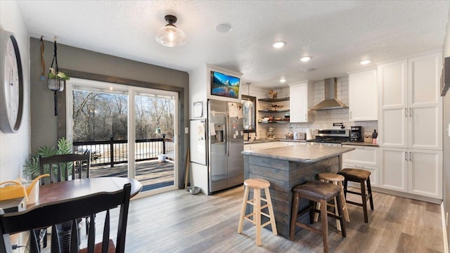 kitchen featuring stainless steel appliances, white cabinetry, light hardwood / wood-style floors, and wall chimney exhaust hood