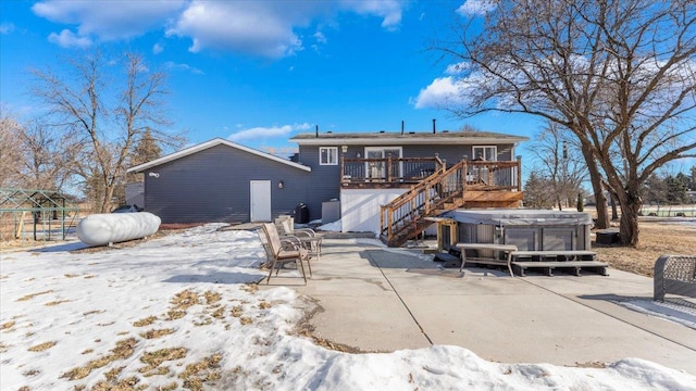 snow covered rear of property featuring a wooden deck, a hot tub, and a patio