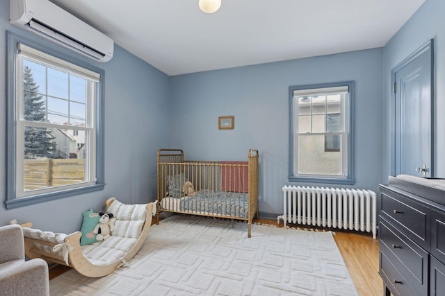 bedroom with radiator, a wall mounted air conditioner, light hardwood / wood-style floors, and a nursery area