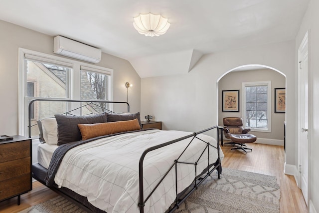 bedroom with lofted ceiling, a wall mounted AC, multiple windows, and light hardwood / wood-style flooring