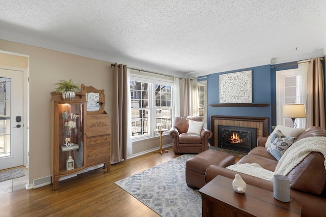 living area with a fireplace, wood finished floors, visible vents, and a textured ceiling