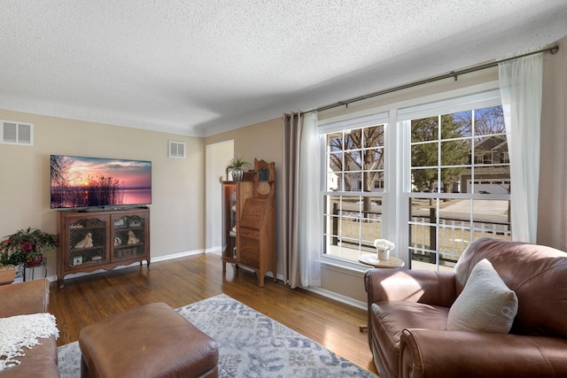 living room featuring wood finished floors, visible vents, and a textured ceiling