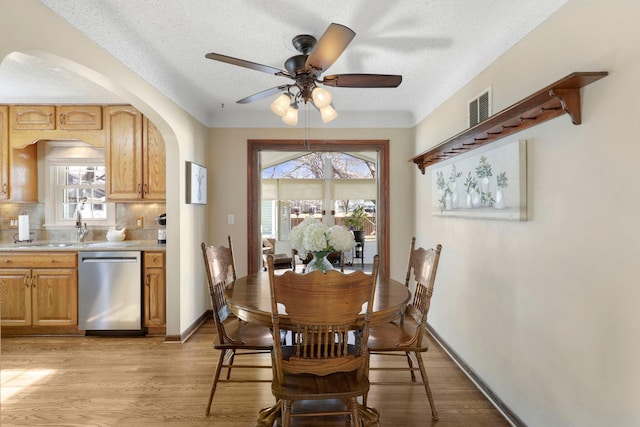 dining space featuring ceiling fan, light wood-style floors, visible vents, and arched walkways