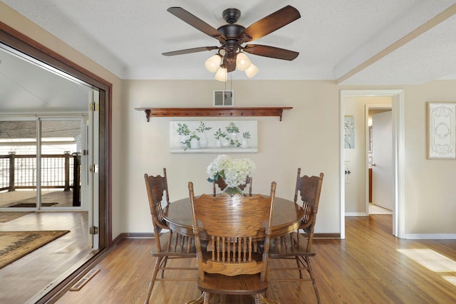 dining room featuring wood finished floors, baseboards, visible vents, ceiling fan, and a textured ceiling