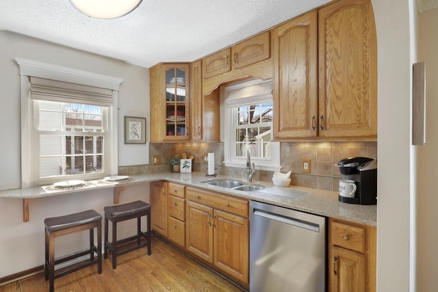 kitchen with decorative backsplash, a sink, stainless steel dishwasher, light wood-style floors, and glass insert cabinets