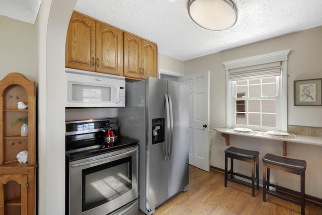 kitchen with light wood-type flooring, light countertops, brown cabinets, appliances with stainless steel finishes, and a textured ceiling