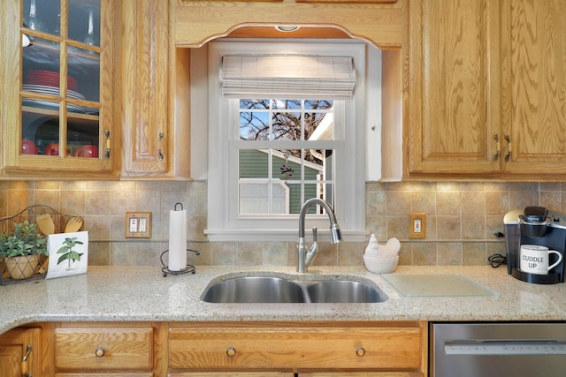 kitchen with a sink, light stone counters, glass insert cabinets, decorative backsplash, and dishwasher