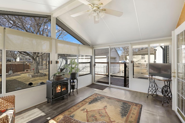 sunroom with lofted ceiling with beams, a wood stove, and a ceiling fan