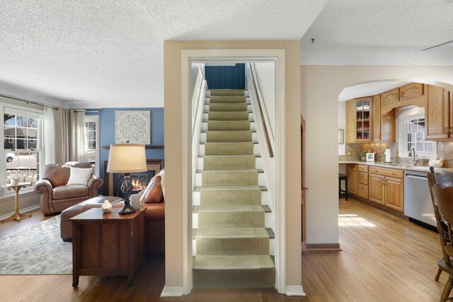 staircase with a textured ceiling, wood finished floors, arched walkways, and baseboards