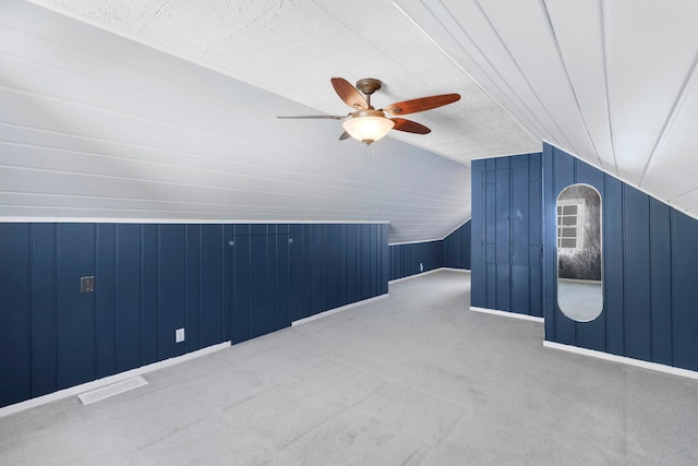 bonus room featuring visible vents, wood walls, lofted ceiling, carpet flooring, and a ceiling fan