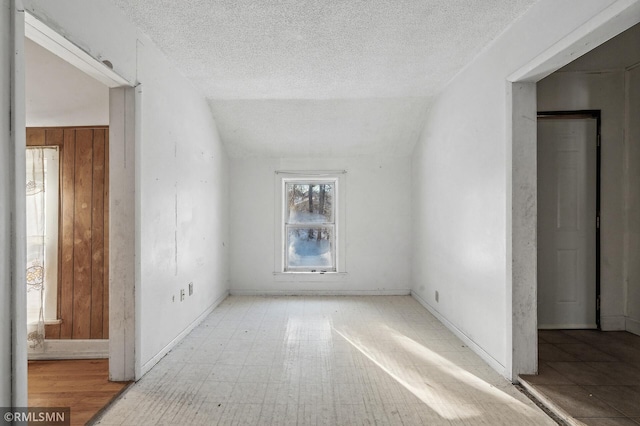 unfurnished room with a textured ceiling and vaulted ceiling