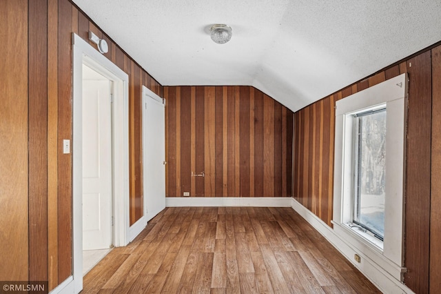 bonus room with a textured ceiling, light wood-type flooring, wooden walls, and vaulted ceiling