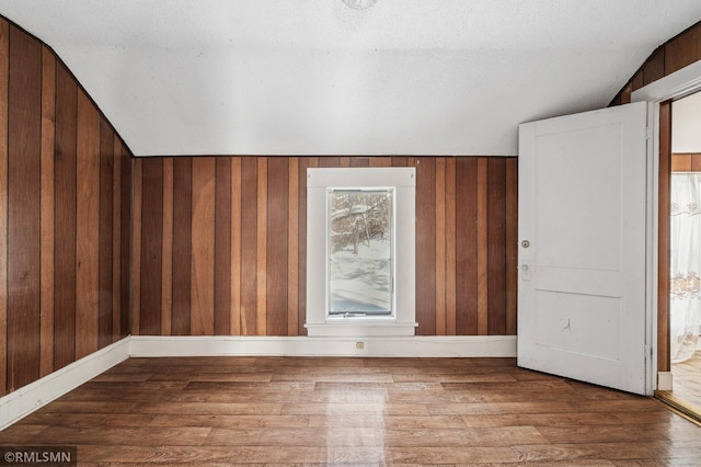 empty room with hardwood / wood-style flooring, wooden walls, and lofted ceiling