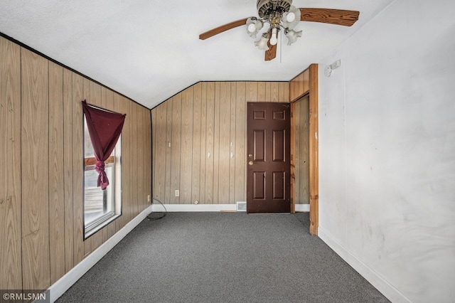 empty room with vaulted ceiling, ceiling fan, wooden walls, and carpet floors