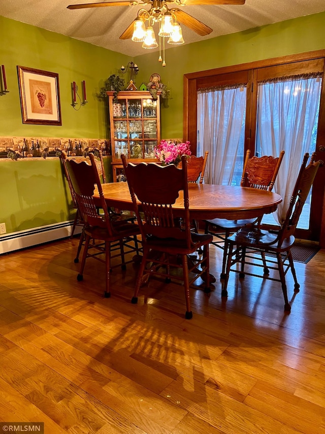 dining area with ceiling fan, a baseboard radiator, a textured ceiling, and wood-type flooring