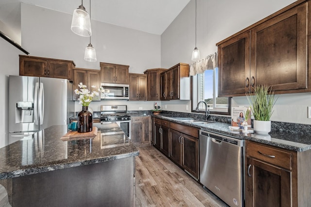 kitchen with sink, hanging light fixtures, stainless steel appliances, high vaulted ceiling, and a kitchen island