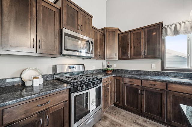 kitchen with sink, dark stone counters, stainless steel appliances, dark brown cabinets, and light hardwood / wood-style flooring