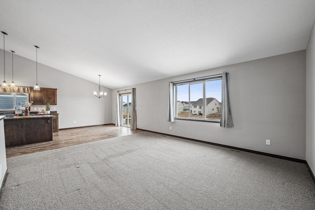 unfurnished living room featuring an inviting chandelier, vaulted ceiling, light colored carpet, and a textured ceiling