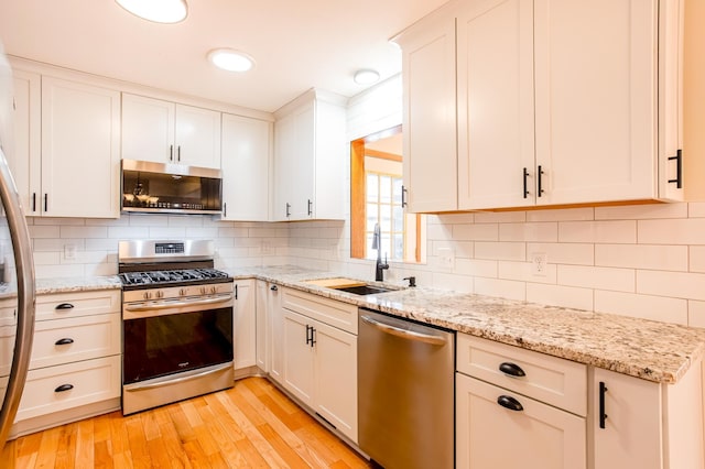 kitchen with white cabinetry, sink, backsplash, stainless steel appliances, and light stone countertops