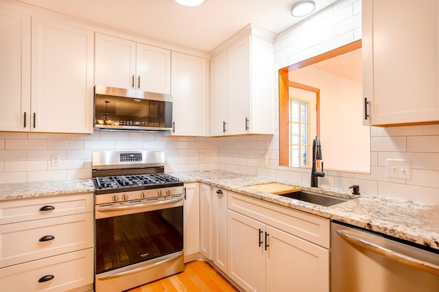 kitchen with stainless steel appliances, tasteful backsplash, sink, and light stone counters