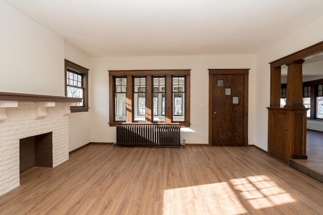 unfurnished living room featuring hardwood / wood-style flooring, a fireplace, radiator, and ornate columns