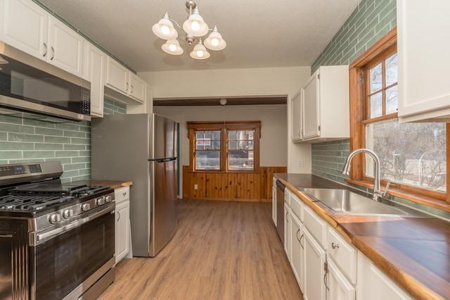 kitchen with white cabinetry, sink, backsplash, stainless steel appliances, and light hardwood / wood-style flooring