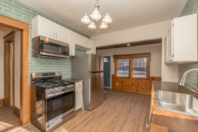 kitchen with stainless steel appliances, sink, pendant lighting, and white cabinets