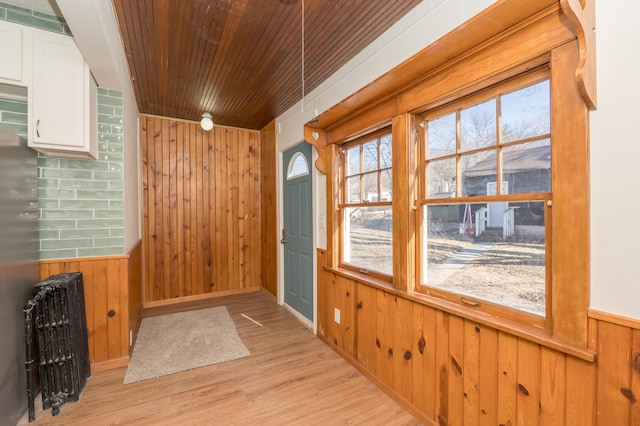 doorway to outside featuring radiator, wooden walls, wood ceiling, and light wood-type flooring