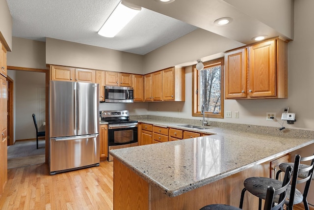 kitchen with sink, a breakfast bar, stainless steel appliances, light stone counters, and kitchen peninsula