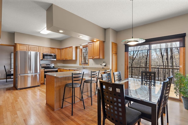 kitchen with appliances with stainless steel finishes, decorative light fixtures, sink, light hardwood / wood-style floors, and a textured ceiling