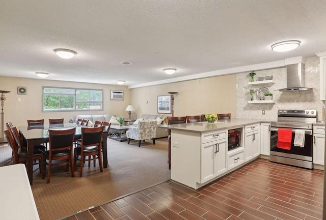 kitchen with stainless steel electric range oven, white cabinetry, wall chimney range hood, black microwave, and kitchen peninsula