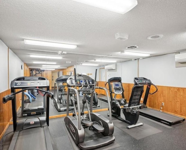 exercise room featuring an AC wall unit, a textured ceiling, and wood walls