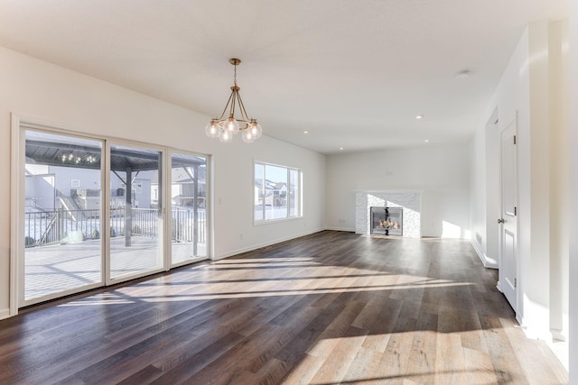 unfurnished living room with a chandelier, a warm lit fireplace, baseboards, and dark wood-style flooring