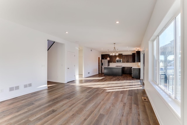 unfurnished living room featuring a wealth of natural light, a notable chandelier, wood finished floors, and recessed lighting