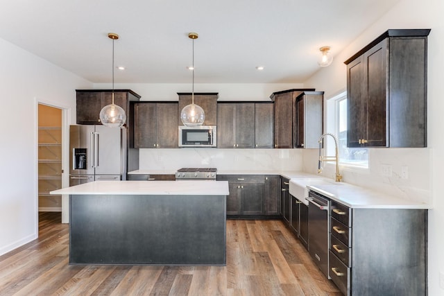 kitchen with stainless steel appliances, a kitchen island, light countertops, and decorative light fixtures