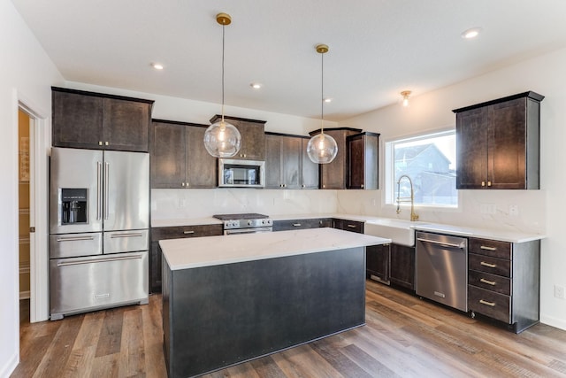 kitchen featuring premium appliances, dark brown cabinetry, a sink, a kitchen island, and pendant lighting