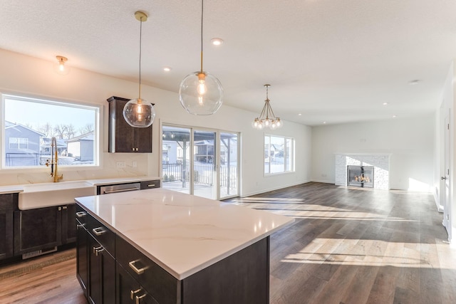 kitchen featuring a warm lit fireplace, wood finished floors, a center island, pendant lighting, and a sink