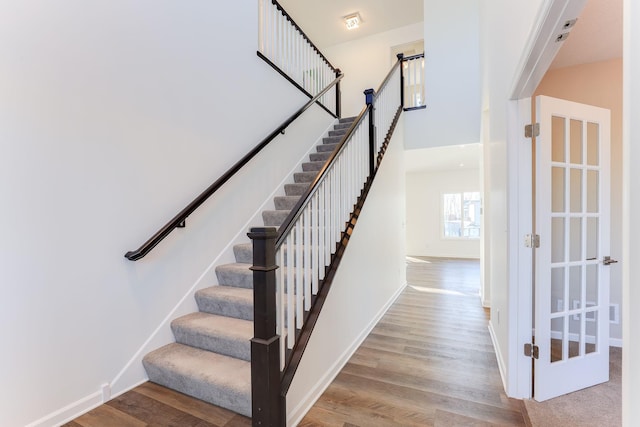 staircase with a high ceiling, wood finished floors, and baseboards