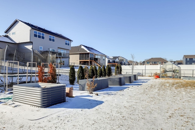 yard layered in snow featuring an outbuilding, fence, a residential view, a trampoline, and an exterior structure