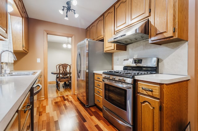 kitchen featuring appliances with stainless steel finishes, decorative backsplash, sink, a chandelier, and light wood-type flooring