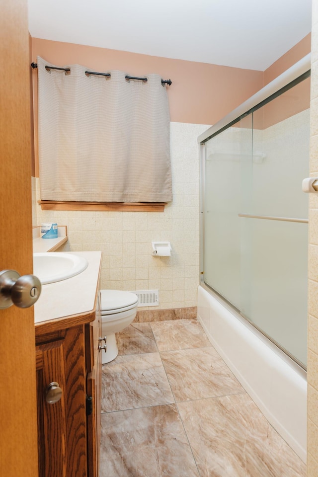 full bathroom featuring toilet, tile walls, shower / bath combination with glass door, and vanity