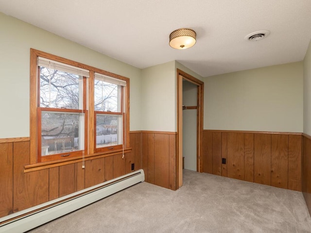 empty room with wooden walls, light colored carpet, and baseboard heating